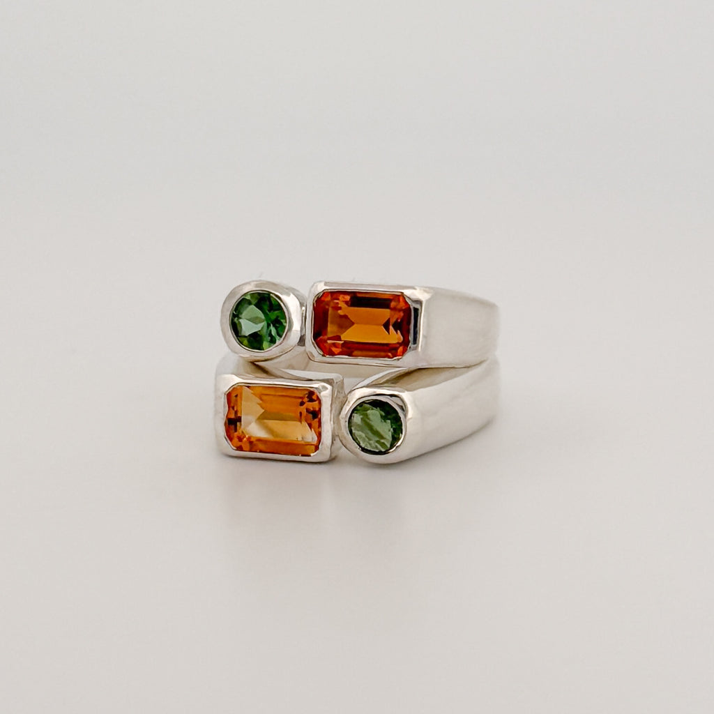 Silver ring with green and orange gemstones on a light gray background