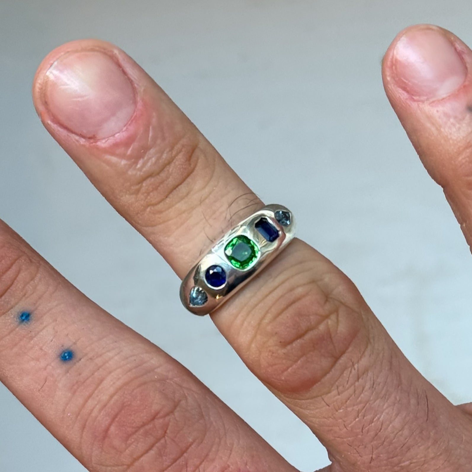 Silver ring with colored stones on a finger against a neutral background