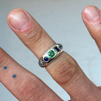 Silver ring with colored stones on a finger against a neutral background