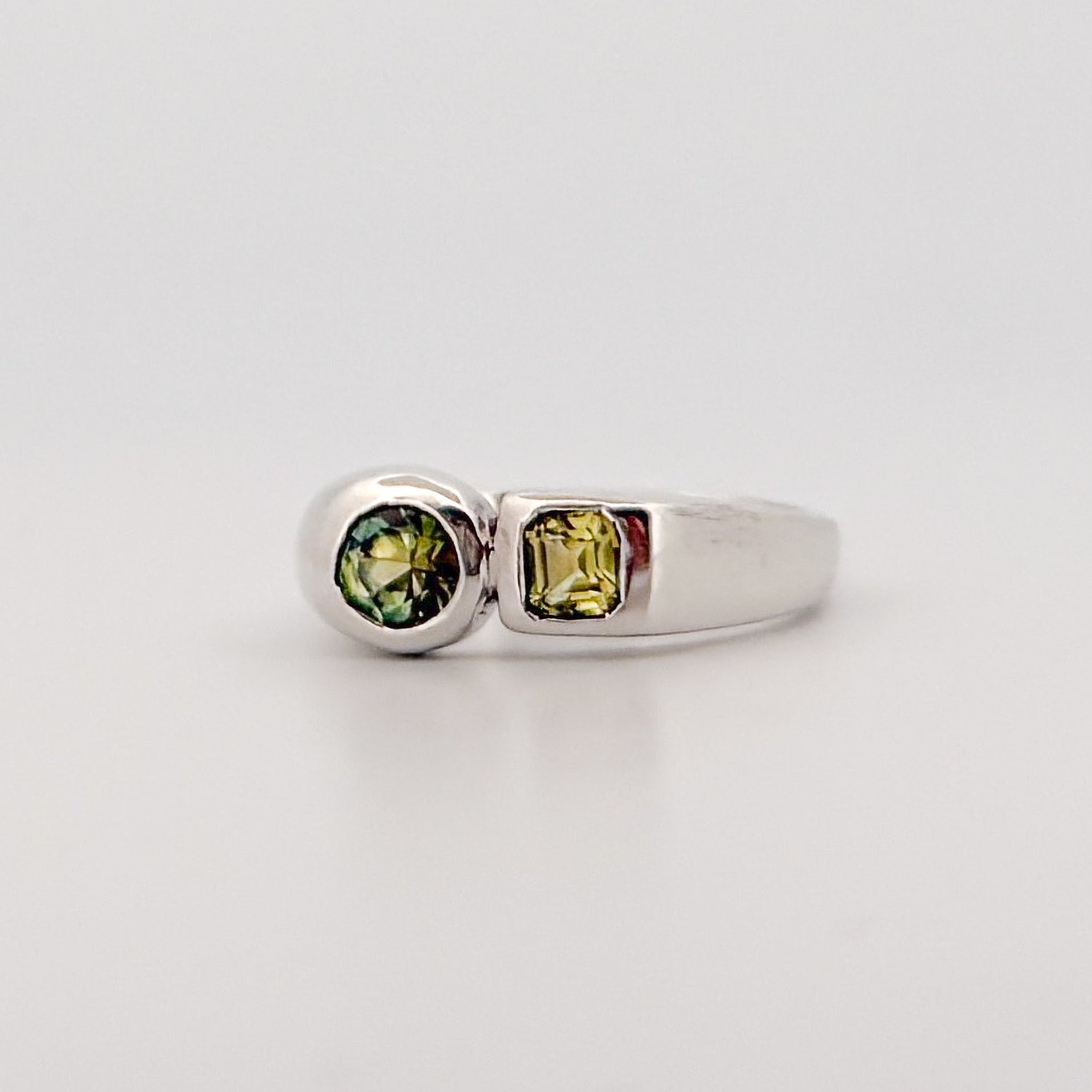 Silver ring with green gemstones on a light gray background
