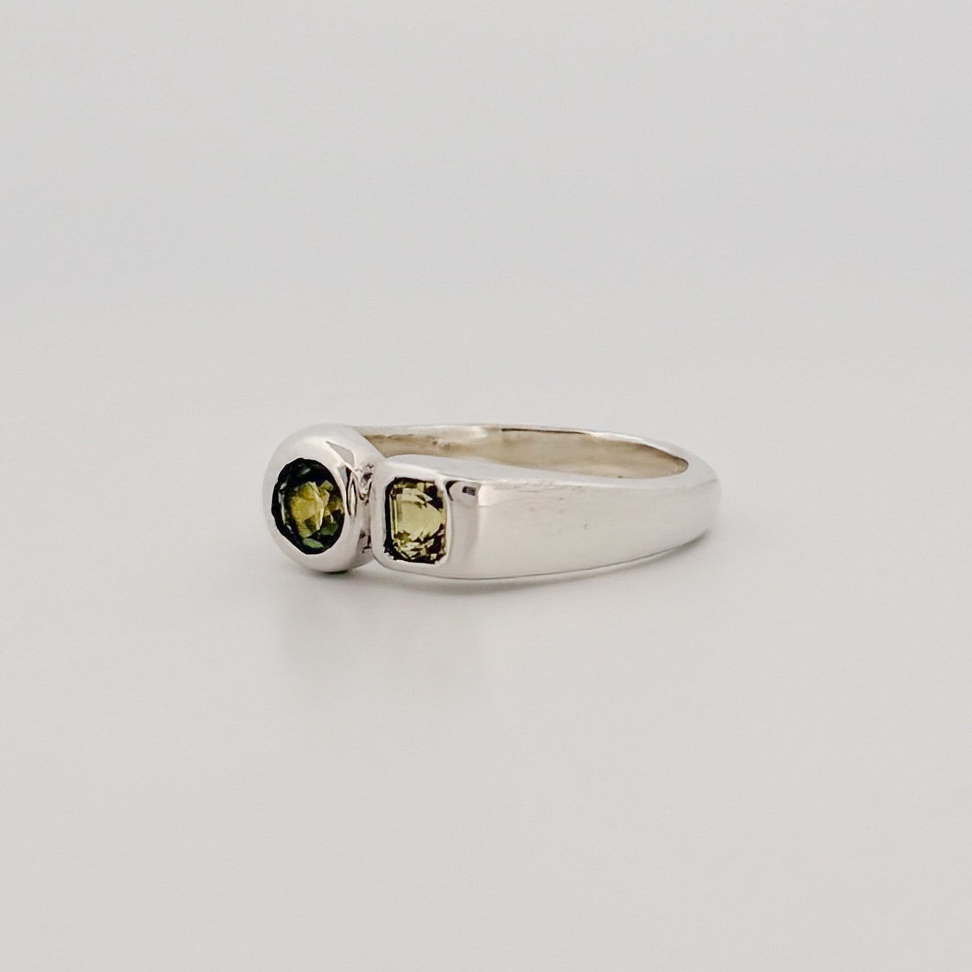 Silver ring with green gemstones on a light gray background