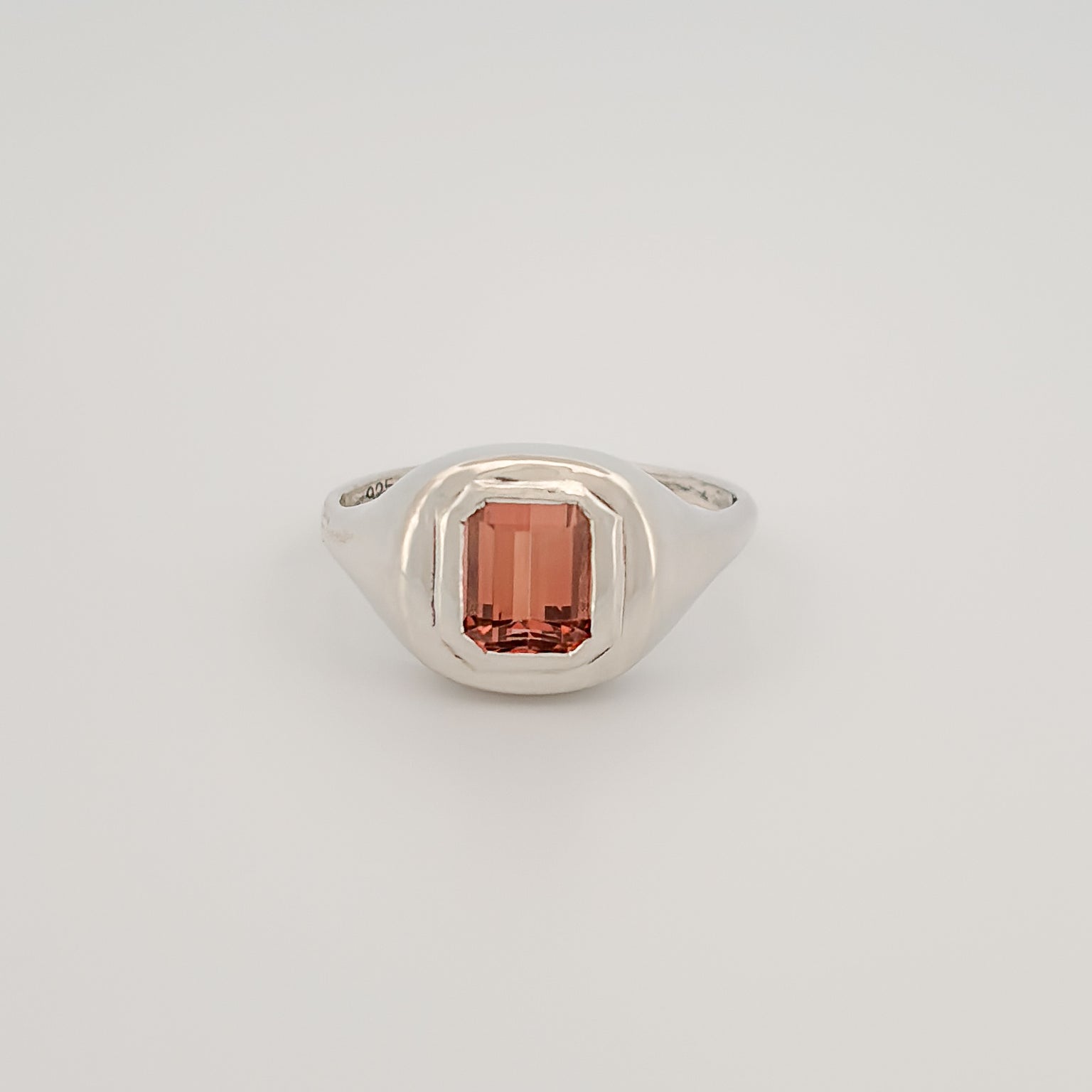 A ring with a rectangular peach tourmaline gemstone set in a silver mounting.