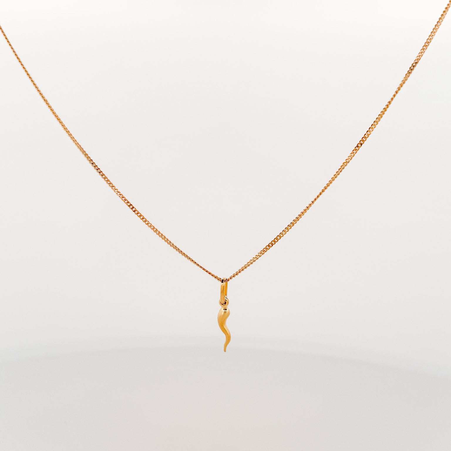 Gold necklace with a chilli pendant on a light gray background