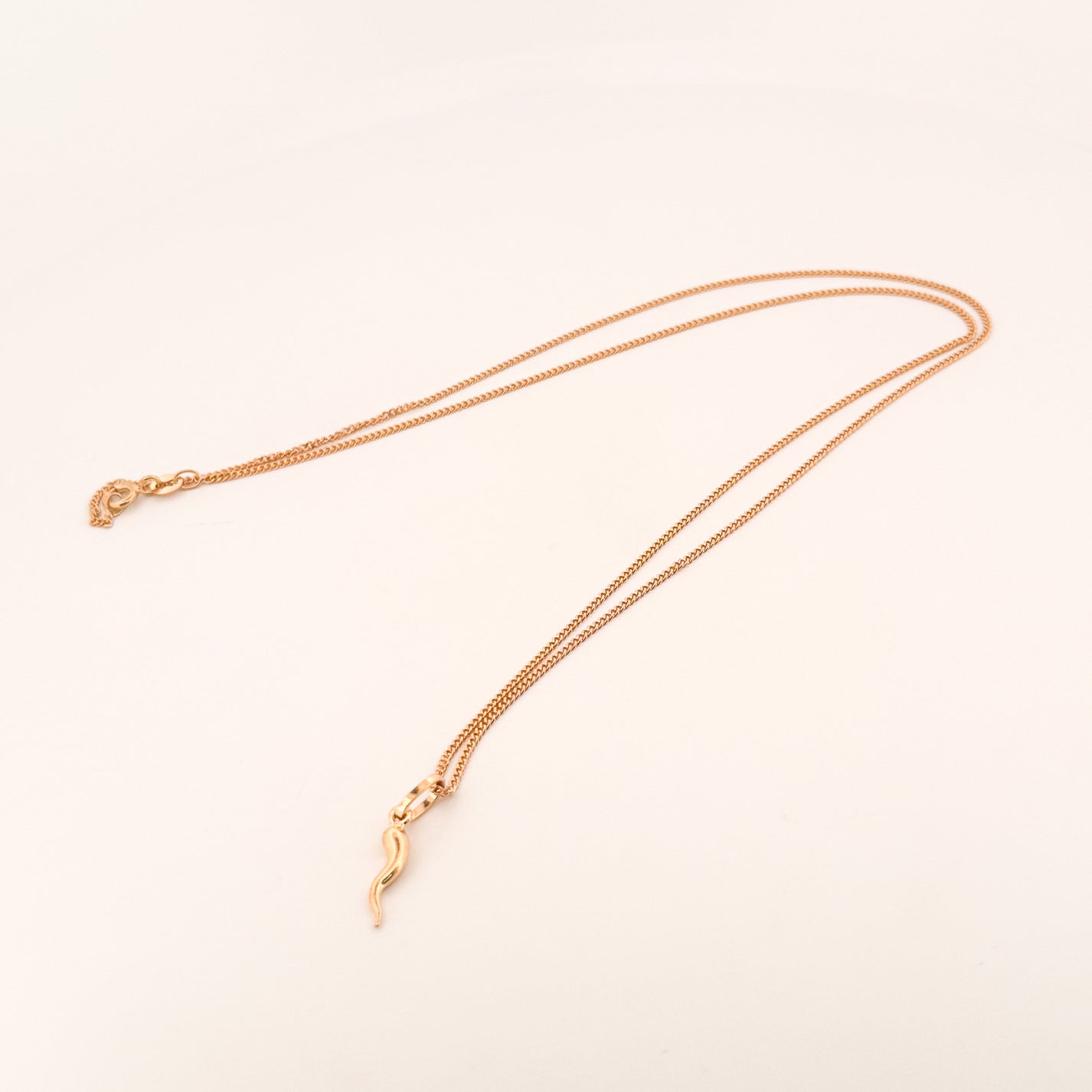 Gold necklace with a delicate pendant on a light beige background
