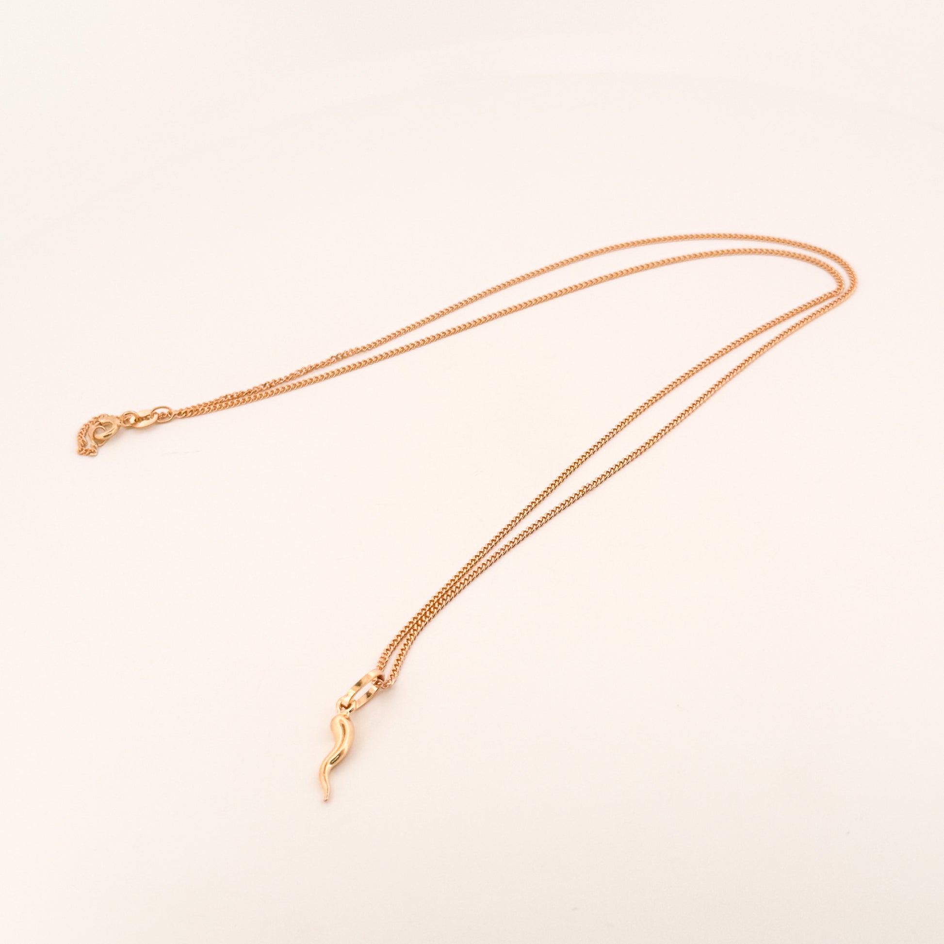 Gold necklace with a delicate pendant on a light beige background