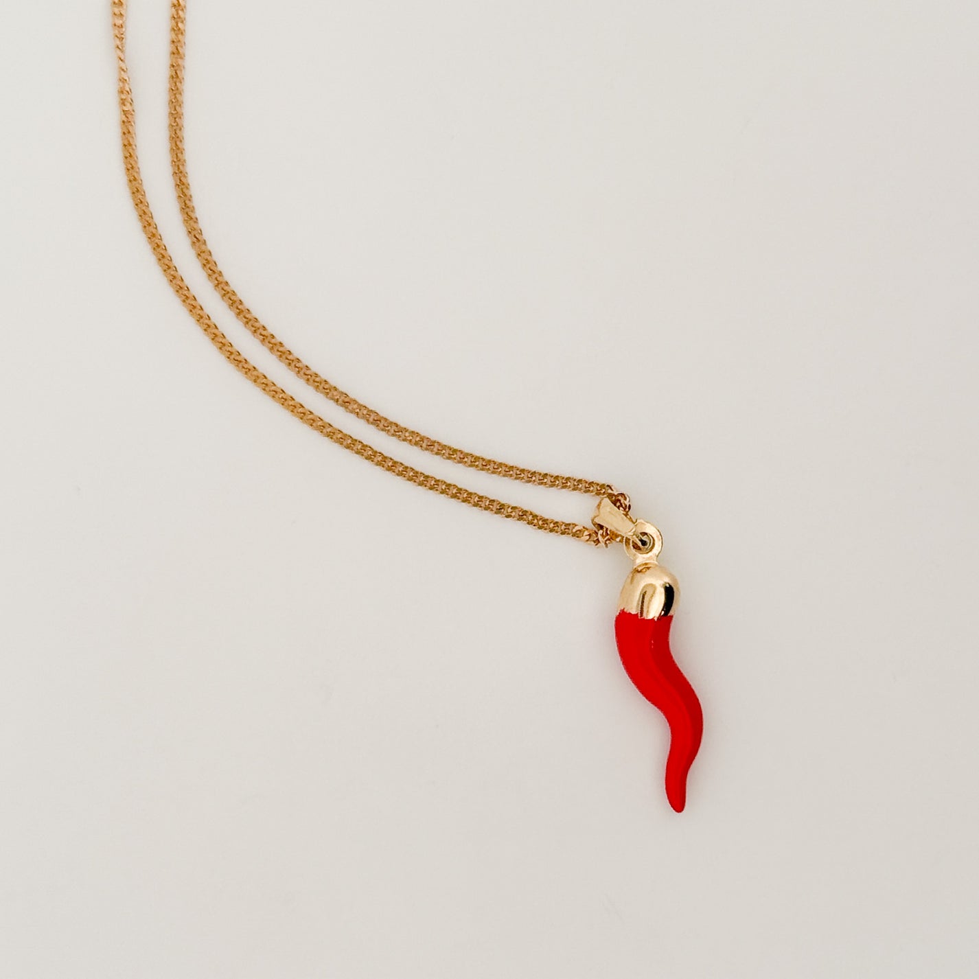 Gold necklace with a red chili pepper pendant on a light gray background