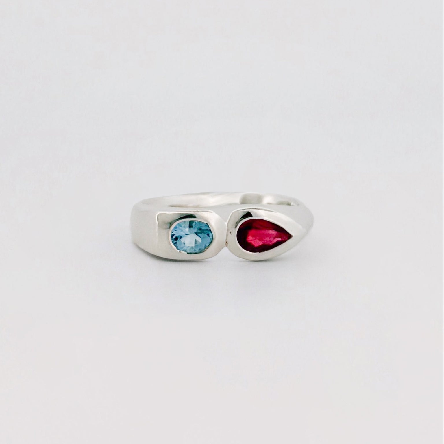 Silver ring with a blue gem and a red gem on a light gray background