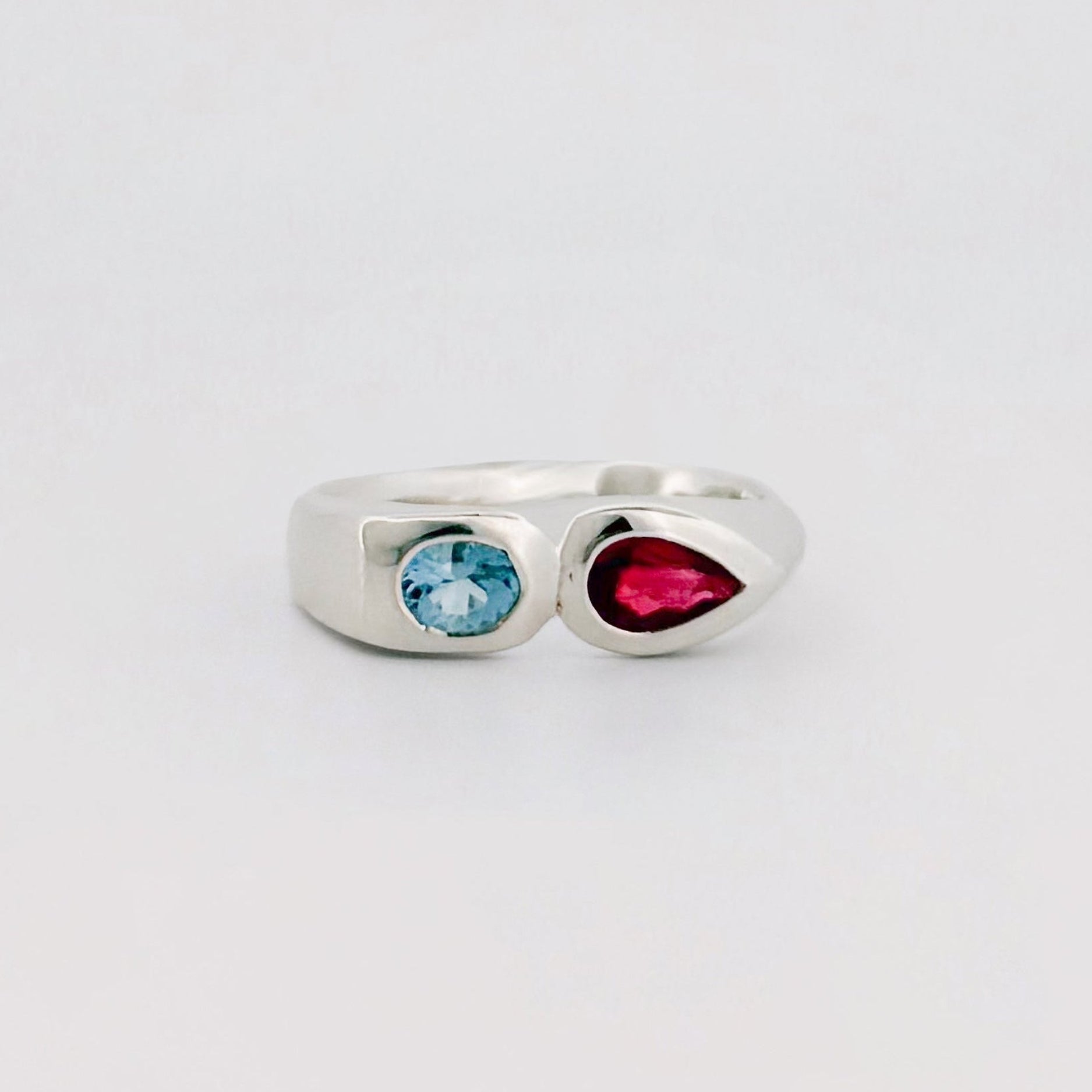 Silver ring with a blue gem and a red gem on a light gray background