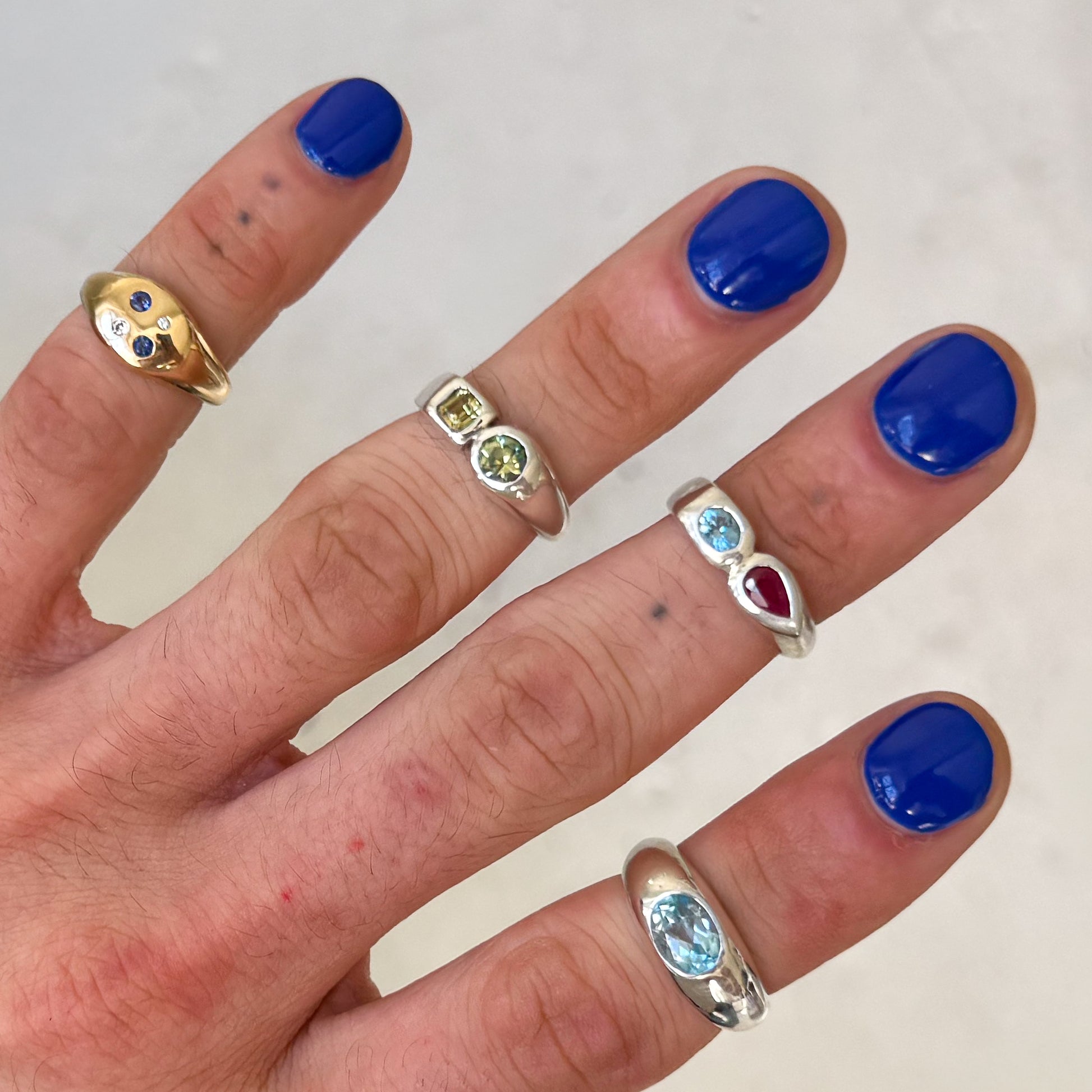 Hand with blue nail polish wearing multiple rings on a plain background