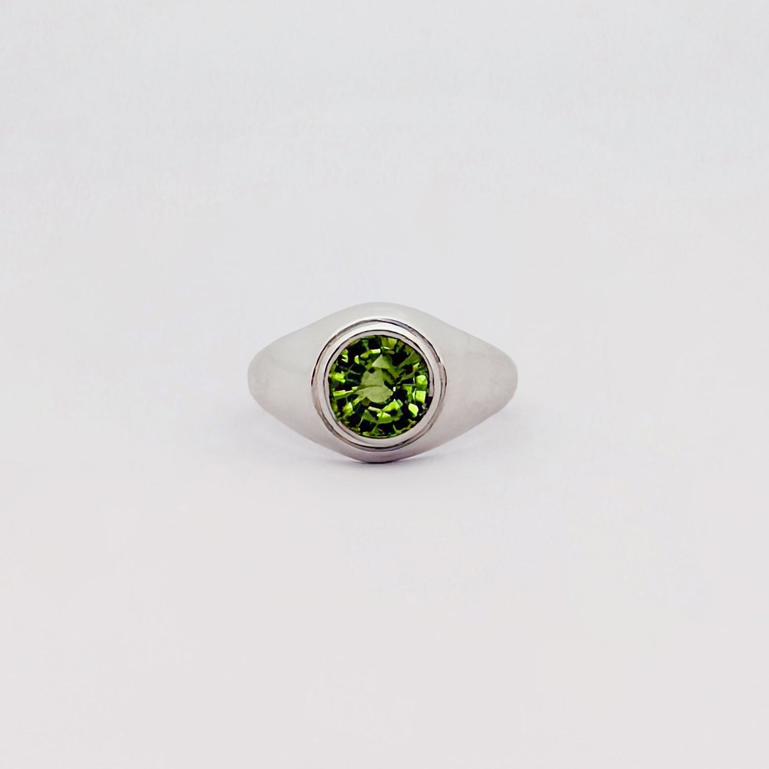 Silver ring with a green gemstone on a light gray background