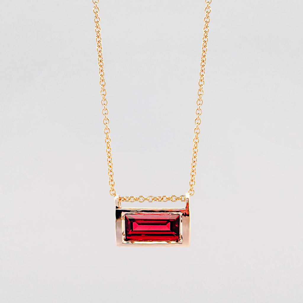 Gold necklace with a red gemstone pendant on a light gray background