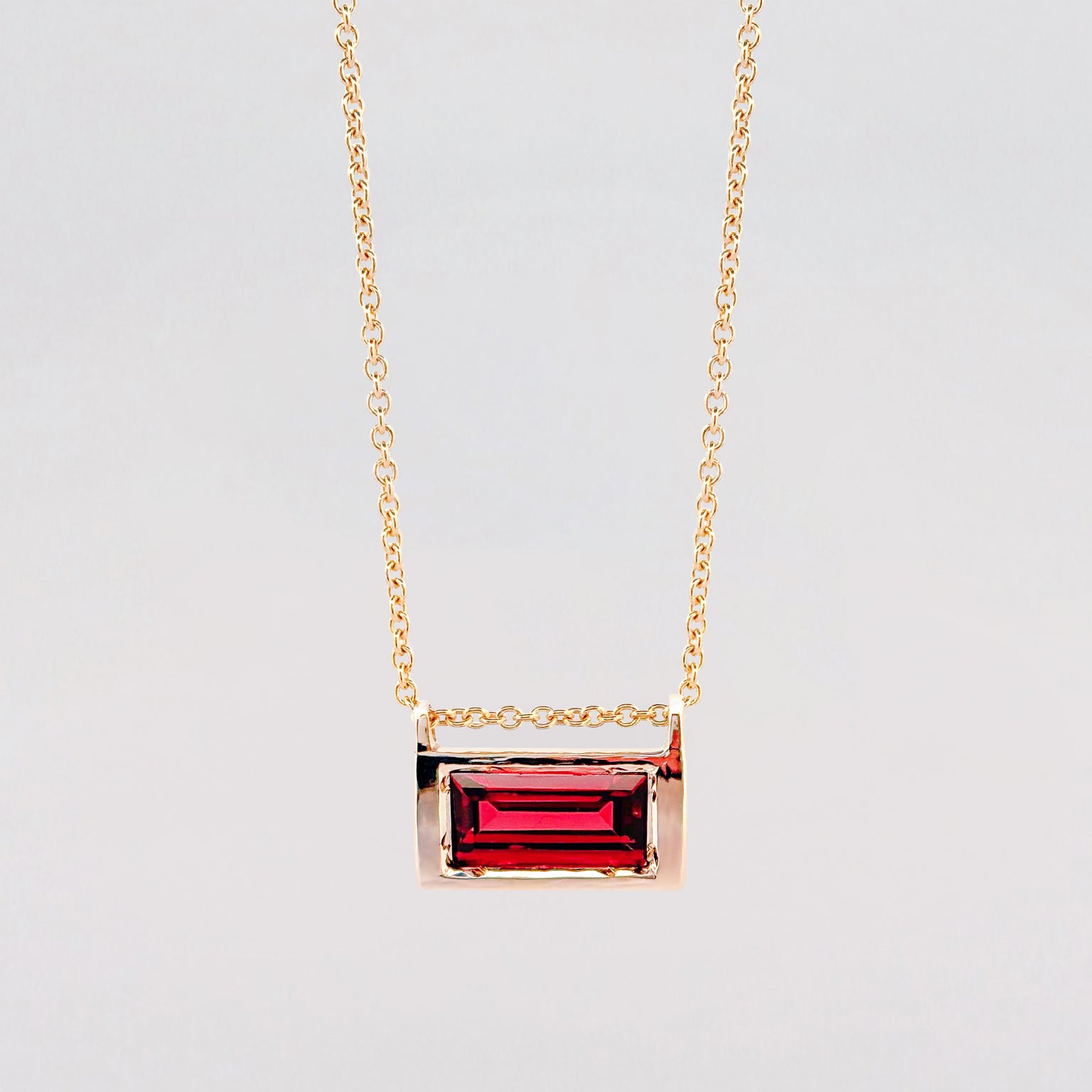 Gold necklace with a red gemstone pendant on a light gray background