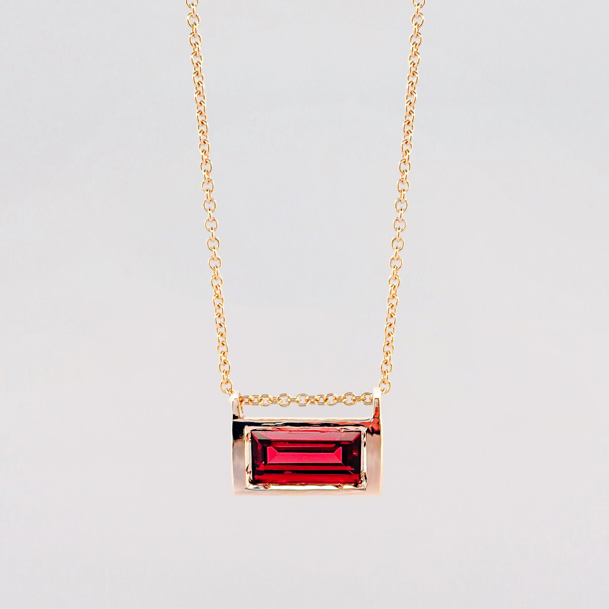 Gold necklace with a red gemstone pendant on a light gray background
