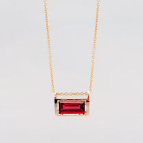 Gold necklace with a red gemstone pendant on a light gray background